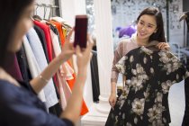 Chinese female friends trying on dress and taking photo in clothing store — Stock Photo