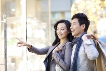 Mulher chinesa apontando para a janela da loja enquanto passeia com o homem — Fotografia de Stock