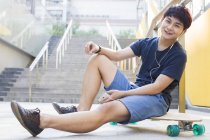 Uomo cinese seduto su skateboard e ascoltare musica — Foto stock