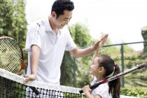 Chinese father doing high-five with daughter on tennis court — Stock Photo