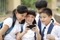 Chinese schoolchildren using smartphone in school yard — Stock Photo