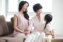 Три поколения китайских женщин сидят и разговаривают на диване — стоковое фото