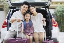 Chinese family sitting with luggage in car trunk — Stock Photo
