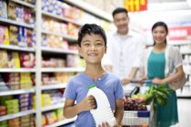 Китайский мальчик с родителями держит бутылку молока в супермаркете — стоковое фото