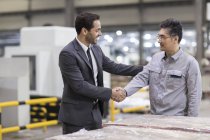 Businessman and engineer shaking hands in factory — Stock Photo