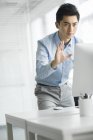 Chinese businessman waving and looking at computer monitor in office — Stock Photo