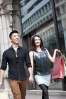 Chinese couple with shopping bags walking in street — Stock Photo