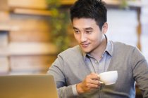 Chinese man using laptop and drinking coffee in coffee shop — Stock Photo