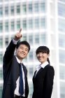 Chinese businessman pointing with businesswoman in front of skyscraper — Stock Photo