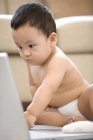 Bebê chinês sentado no chão e olhando para a tela do laptop — Fotografia de Stock