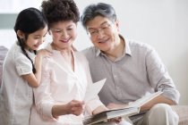 Abuelos chinos y nieta mirando álbum de fotos - foto de stock