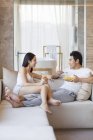 Casal chinês conversando enquanto café da manhã no sofá — Fotografia de Stock