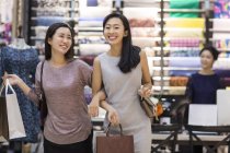 Chinese female friends walking hand in hand in clothing store — Stock Photo