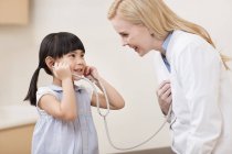 Doctora y niña con estetoscopio - foto de stock