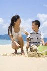 Mother and son playing with sand on beach — Stock Photo
