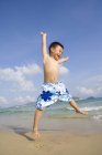 Happy kid jumping with arms outstretched at beach — Stock Photo