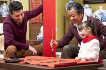 Девочка с отцом и дедушкой занимается китайской каллиграфией — стоковое фото