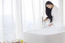 Mulher chinesa que enche a banheira e verifica a água — Fotografia de Stock