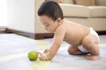 Bambino cinese strisciare e giocare con mela verde su tappeto — Foto stock