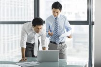 Empresários chineses usando laptop e falando no escritório — Fotografia de Stock