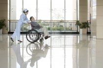 Enfermera china empujando hombre mayor en silla de ruedas - foto de stock