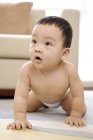 Chinese baby boy crawling on floor in living room, front view — Stock Photo
