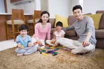 Chinesische Familie mit zwei Kindern spielt Bauklötze auf Teppich — Stockfoto