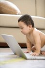 Bebê chinês sentado no chão e olhando para a tela do laptop — Fotografia de Stock