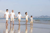 Familia china cogida de la mano y caminando en la playa - foto de stock