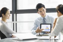 Hombre de negocios chino que presenta gráfico en la pantalla digital de la tableta en la oficina - foto de stock