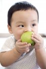 Chinese infant eating green apple and looking away — Stock Photo