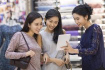 Chinese female friends using digital tablet in clothing store — Stock Photo
