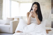 Mujer china usando teléfono inteligente en la cama por la mañana - foto de stock