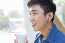 Chinese man drinking coffee and listening music in earphones — Stock Photo
