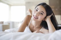 Chinesin liegt auf Bett und stützt sich auf Ellbogen — Stockfoto