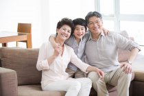 Chinese grandparents and grandson sitting on sofa in home interior — Stock Photo