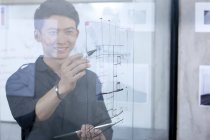 Chinese male designer drawing sketch on glass wall — Stock Photo