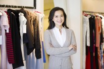 Chinese woman standing with arms crossed in clothing store — Stock Photo