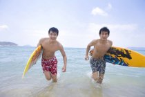 Amigos chineses correndo com pranchas de surf na água do mar — Fotografia de Stock