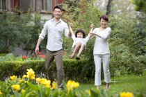 Genitori cinesi che si tengono per mano con il figlio oscillante nel giardino della città — Foto stock