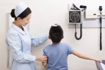 Infirmière chinoise mesurant garçon en salle d'examen — Photo de stock