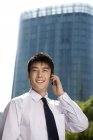 Hombre de negocios chino hablando por teléfono en frente de rascacielos - foto de stock