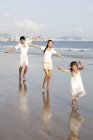 Familia china corriendo en la playa con los brazos extendidos - foto de stock
