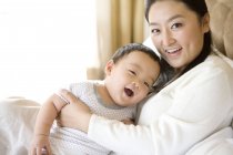 Femme chinoise tenant bébé sur la poitrine et souriant — Photo de stock