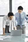 Китайские бизнесмены используют ноутбук и разговаривают в офисе — стоковое фото