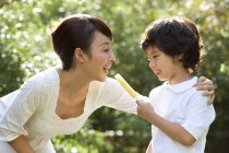 Chinese boy sharing ice pop with mother outdoors — Stock Photo