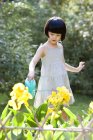 Pequena menina chinesa regando flores no jardim — Fotografia de Stock