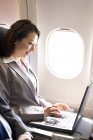Femme d'affaires chinoise utilisant un ordinateur portable dans l'avion — Photo de stock