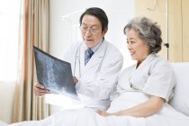 Médico chino mostrando imagen de rayos X al paciente - foto de stock