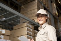 Male Chinese warehouse worker with clipboard looking in camera — Stock Photo